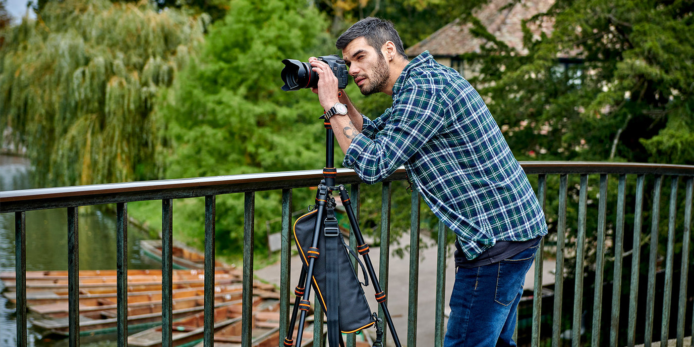 Man taking a photograph with a camera on a tripod by a lake